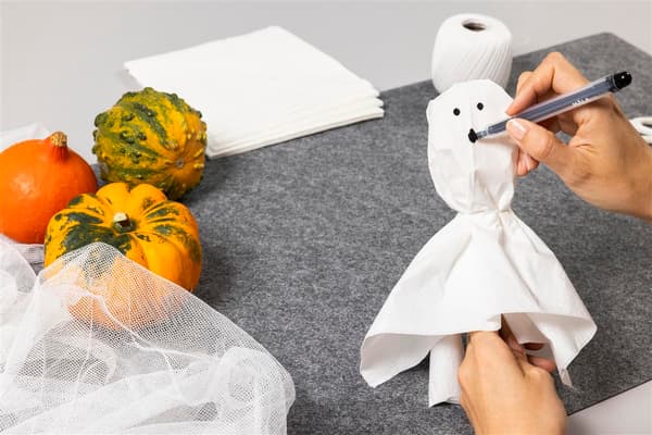 Die Frau wickelt ein Tuch um den Löffel und malt ein Gesicht darauf.
