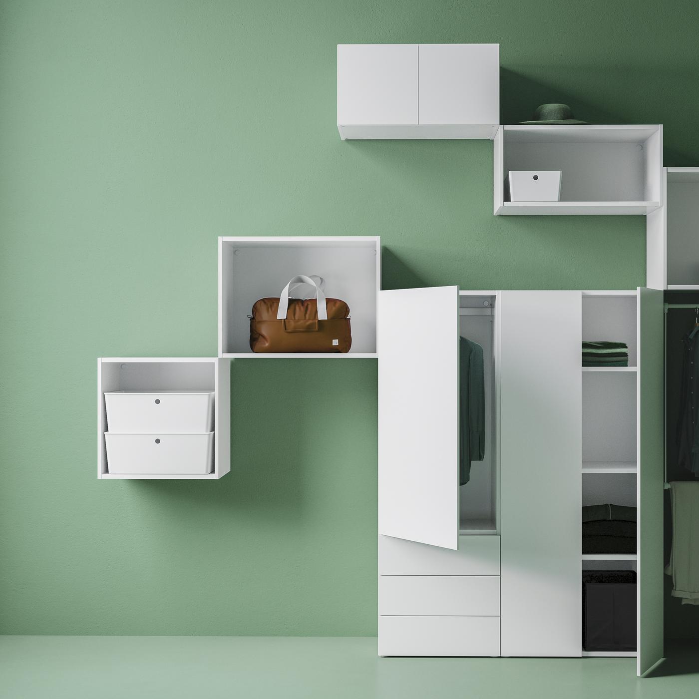 Different sizes of white PLATSA storage units placed on a green wall, with some doors open revealing folded and hung clothes.