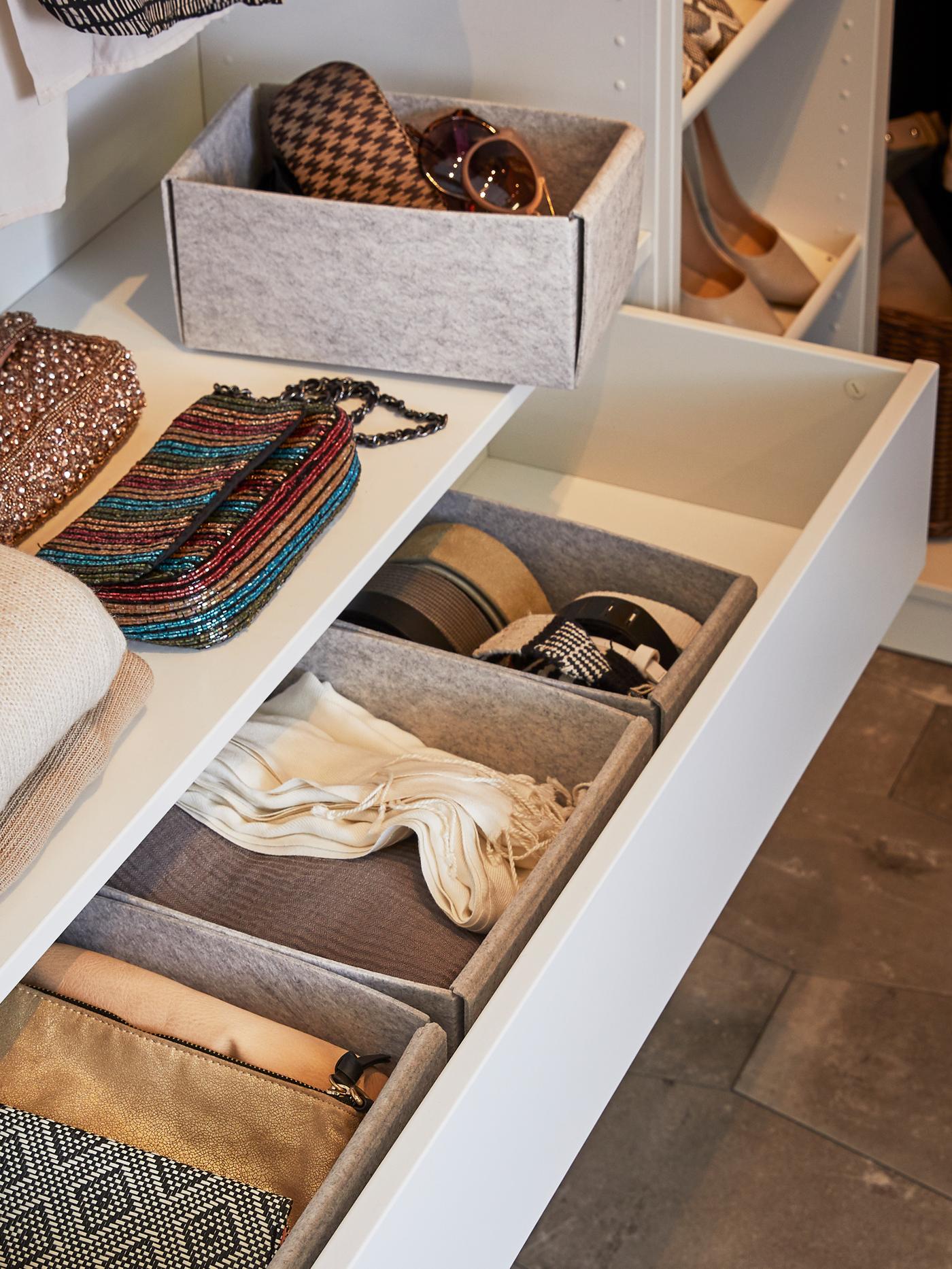 Différents accessoires vestimentaires dans des boîtes KOMPLEMENT grises insérées dans un tiroir KOMPLEMENT blanc ouvert et sur la tablette située au-dessus.