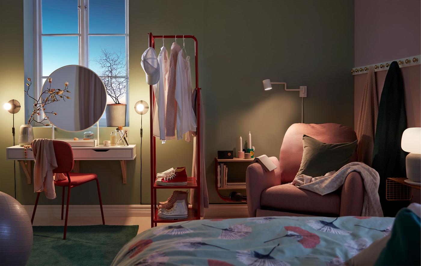 Dimly lit bedroom with a make-up nook, room-dividing clothes rack and reading corner with recliner.