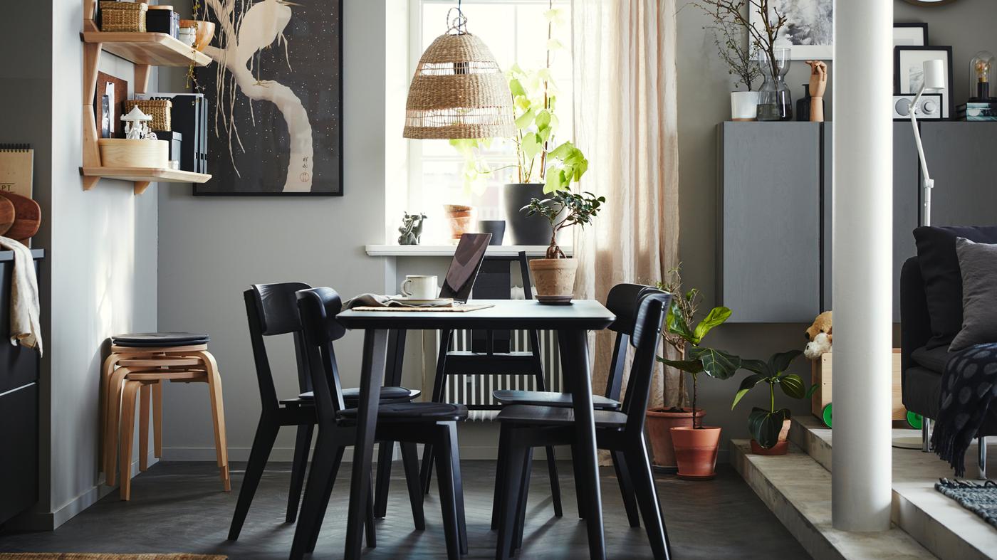 Dining area with a table, four chairs and a highchair in black, open shelves in ash veneer, four stools and beige curtains.