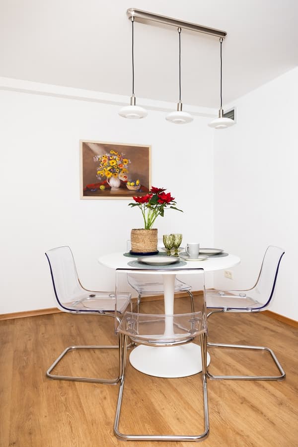 Dining area with round white table, four transparent chairs, and floral wall painting.