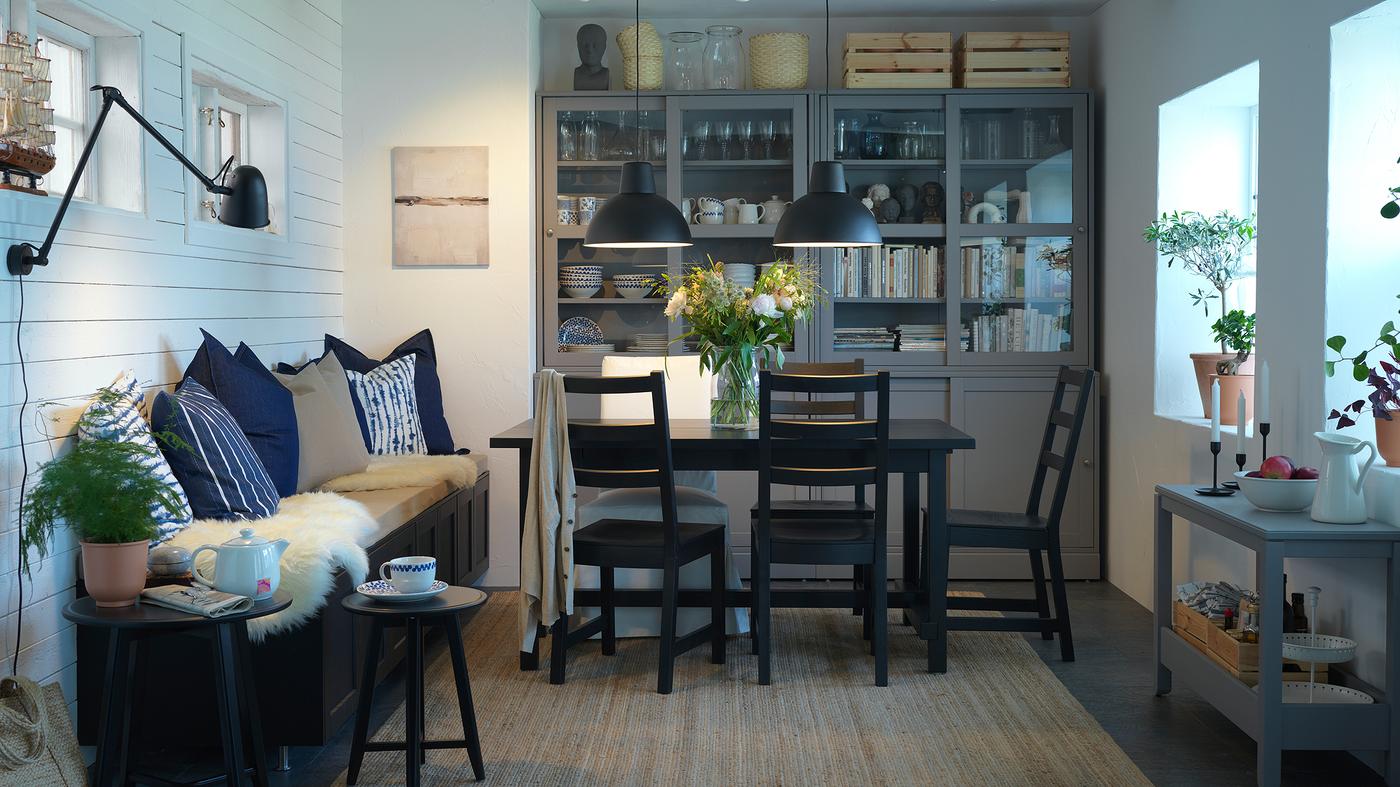 Dining room with a black table and chairs, a jute rug, black pendant lamps and a storage combination with sliding doors.