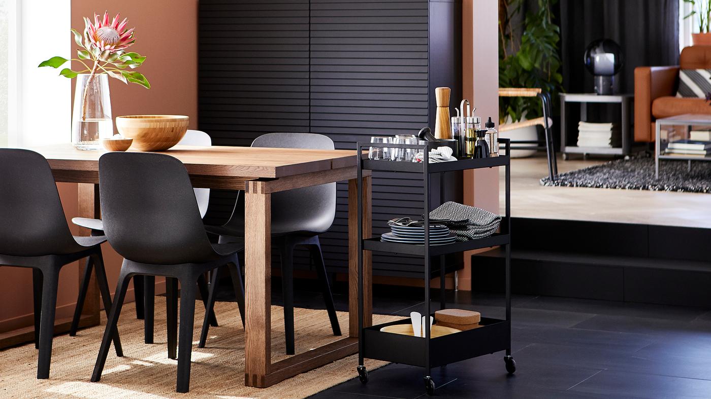 Dining room with anthracite chairs, a stained oak veneer table, black storage, a jute rug and a trolley with tableware.