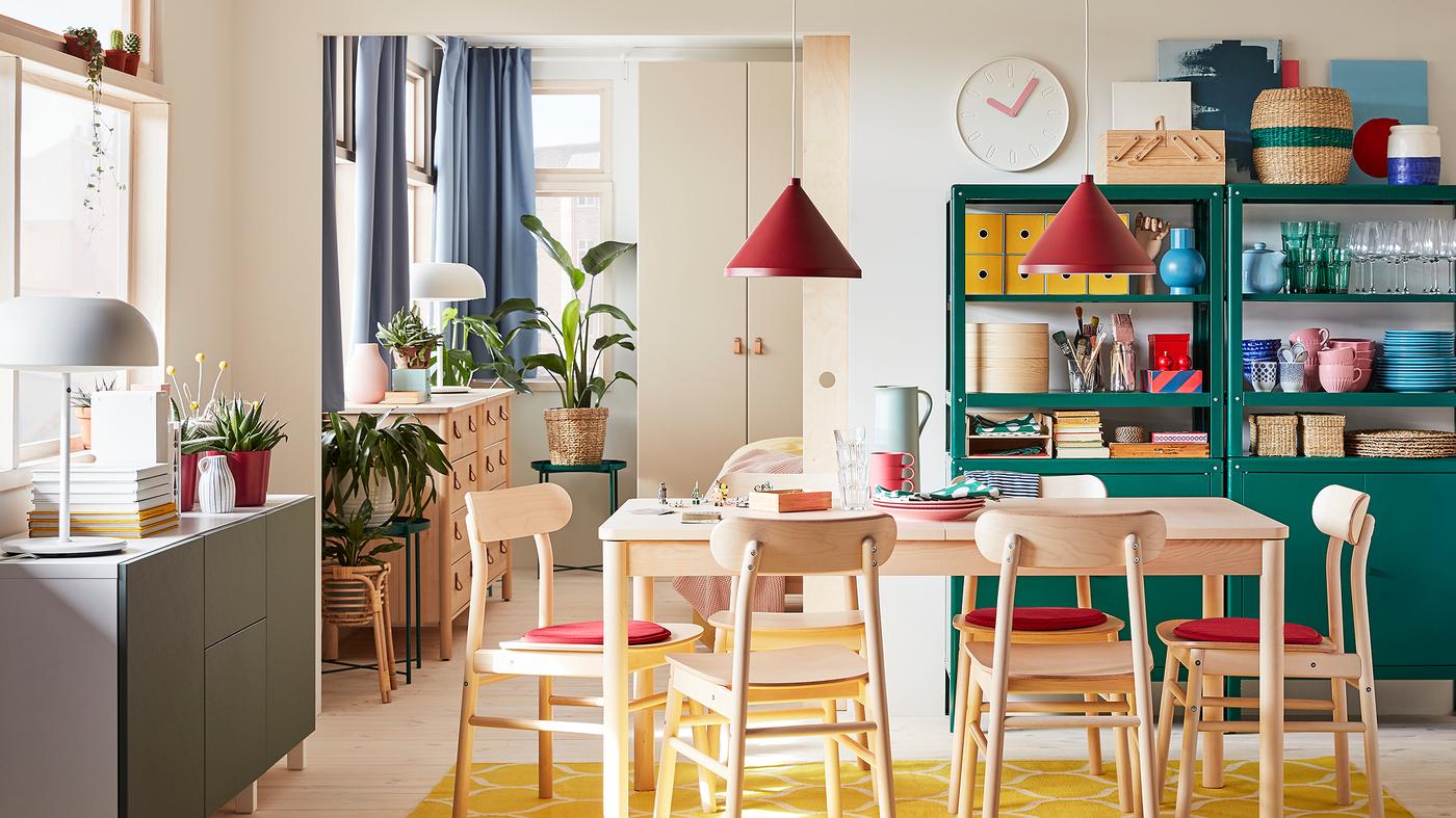 Dining room with table and chairs in birch, a yellow rug, a white/grey-green storage combination and dark red pendant lamps.