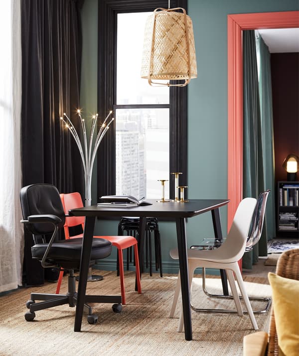 Dining table in living room with odd chairs. Colour palette of rich colours and brighter accents; decorative lighting.