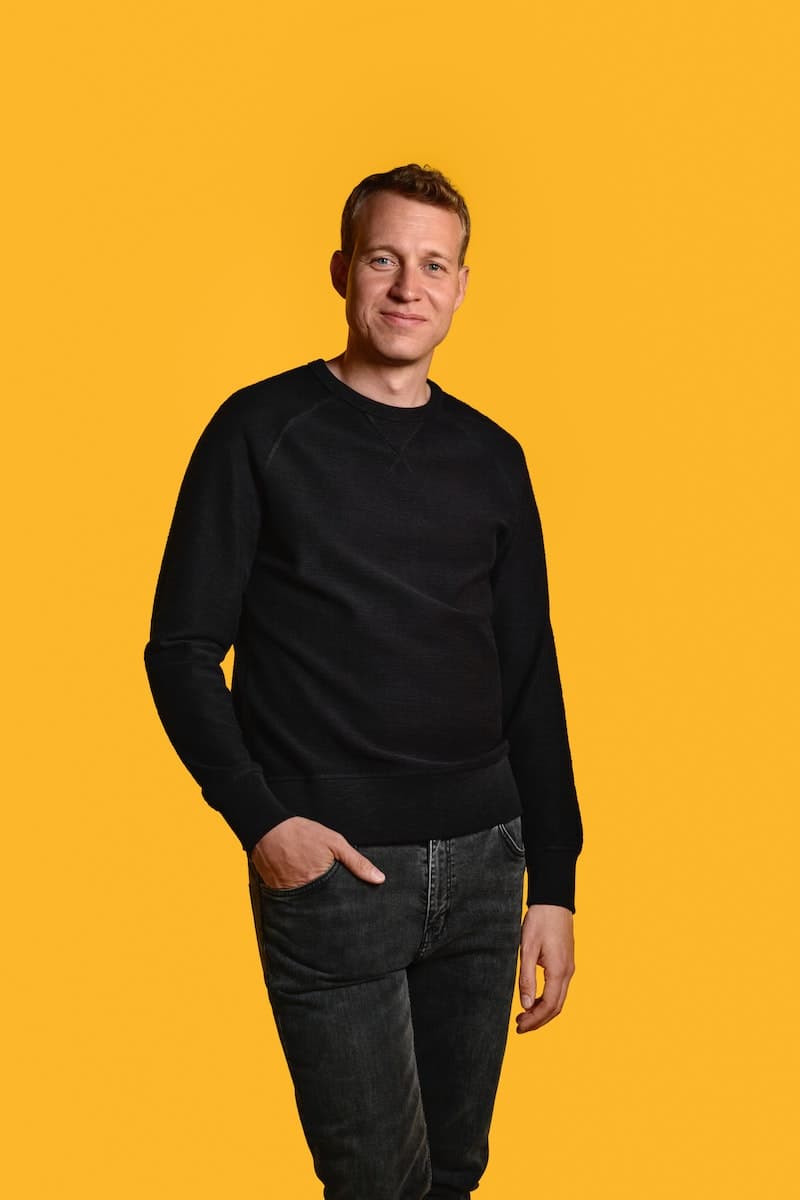Diseñador David Wahl vestido completamente de negro y atrás un fondo amarillo.