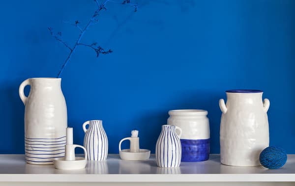Divers vases, des pots et des chandeliers en céramique bleu et crème d’allure rustique placés côte à côte sur une table devant un mur bleu vif.