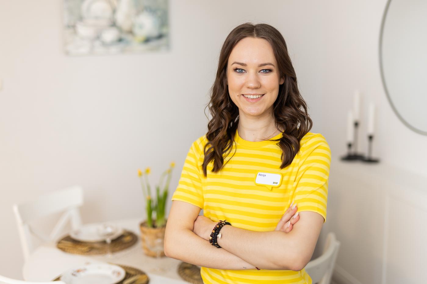 Дизайнер IKEA в жёлтой футболке стоит в светлой комнате и улыбается в камеру.