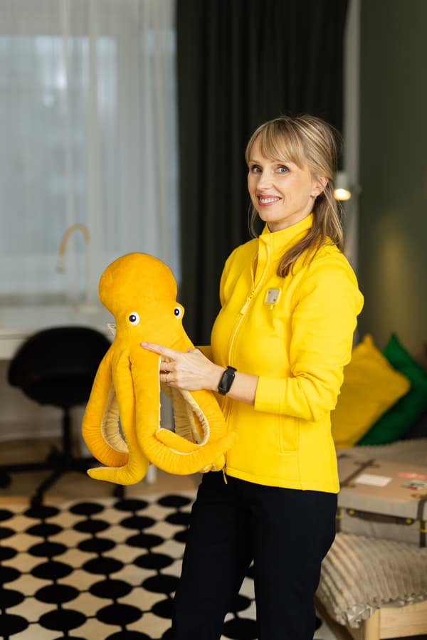 Дизайнер IKEA в жёлтой куртке улыбается в камеру и держит в руках жёлтую игрушку-осьминога.