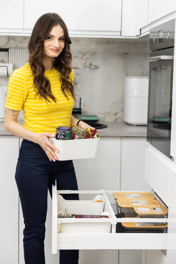 Дизайнер интерьеров IKEA в современной белой кухне открывает ящик с аккуратно организованной посудой и кухонными принадлежностя