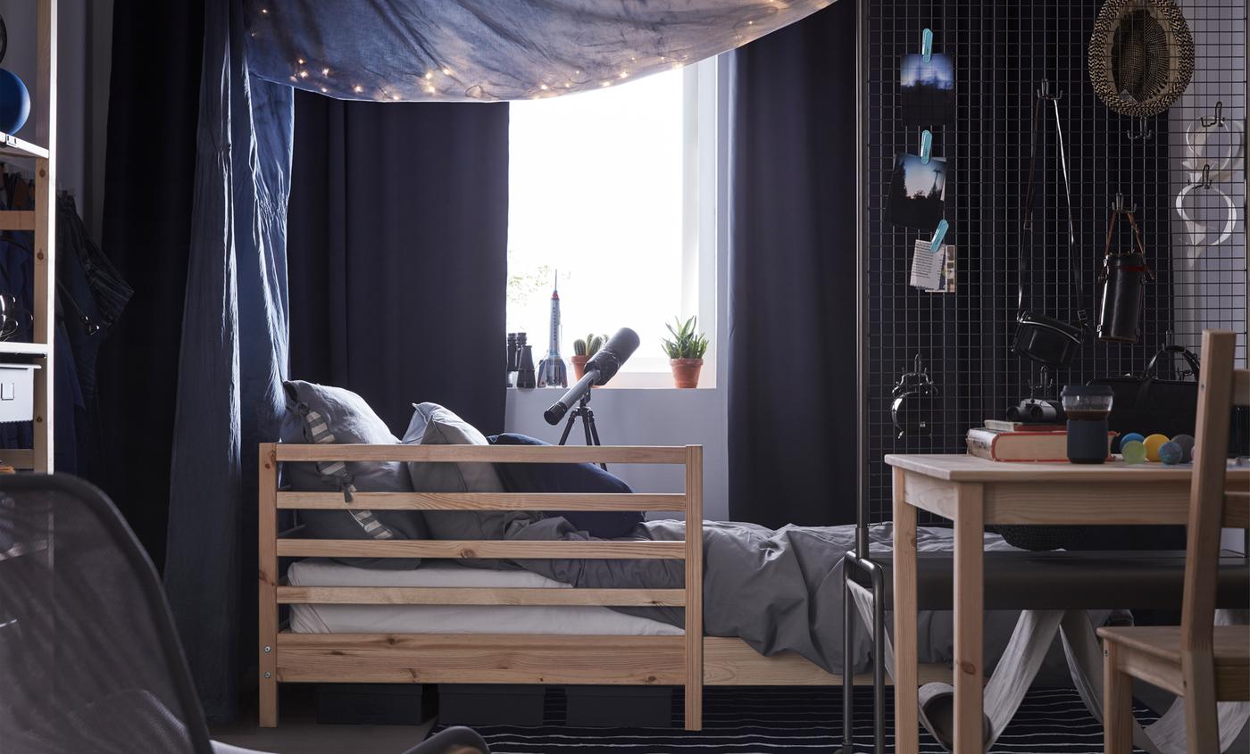Dorm room with a bed, a table and chair and lots of soft textiles.