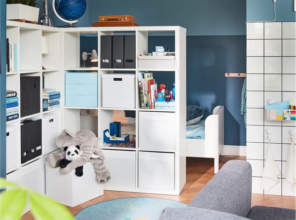 Dos estanterías sirven como separadores de ambientes y ofrecen mucho espacio de almacenamiento. Detrás de ellos, se puede vislumbrar una cama para niños.