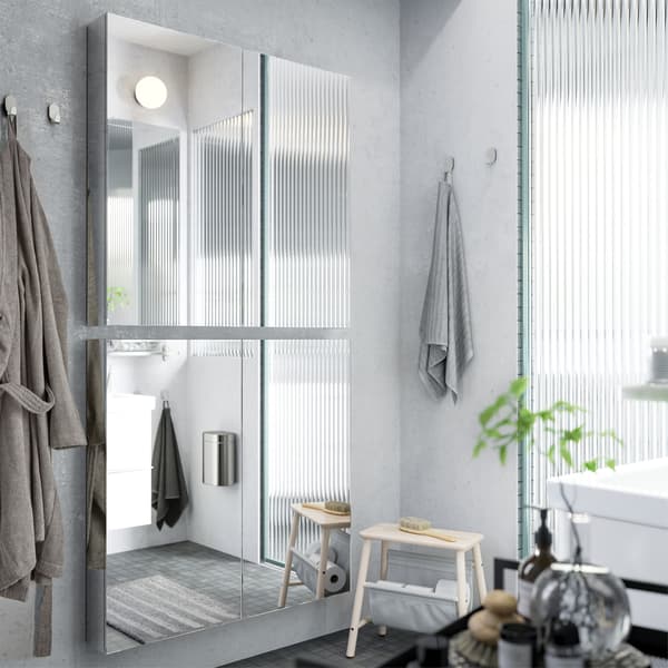 Dos gabinetes con espejo instalados verticalmente en una pared de baño gris para crear un espejo de cuerpo completo.