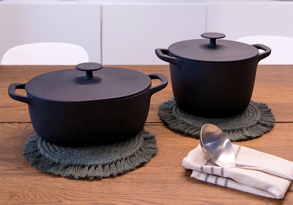 Dos ollas negras sobre soportes para ollas en una mesa.