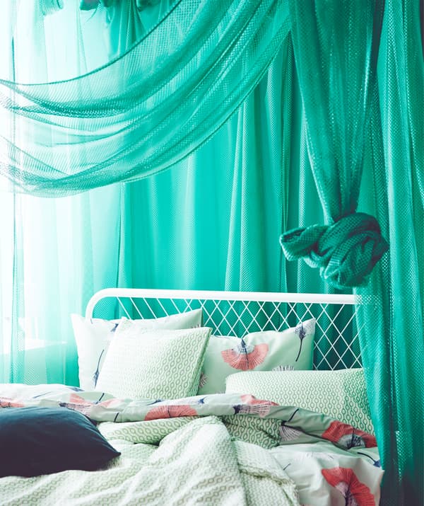 Draped green IKEA GRÅTISTEL net curtains letting through a little light in a bedroom.
