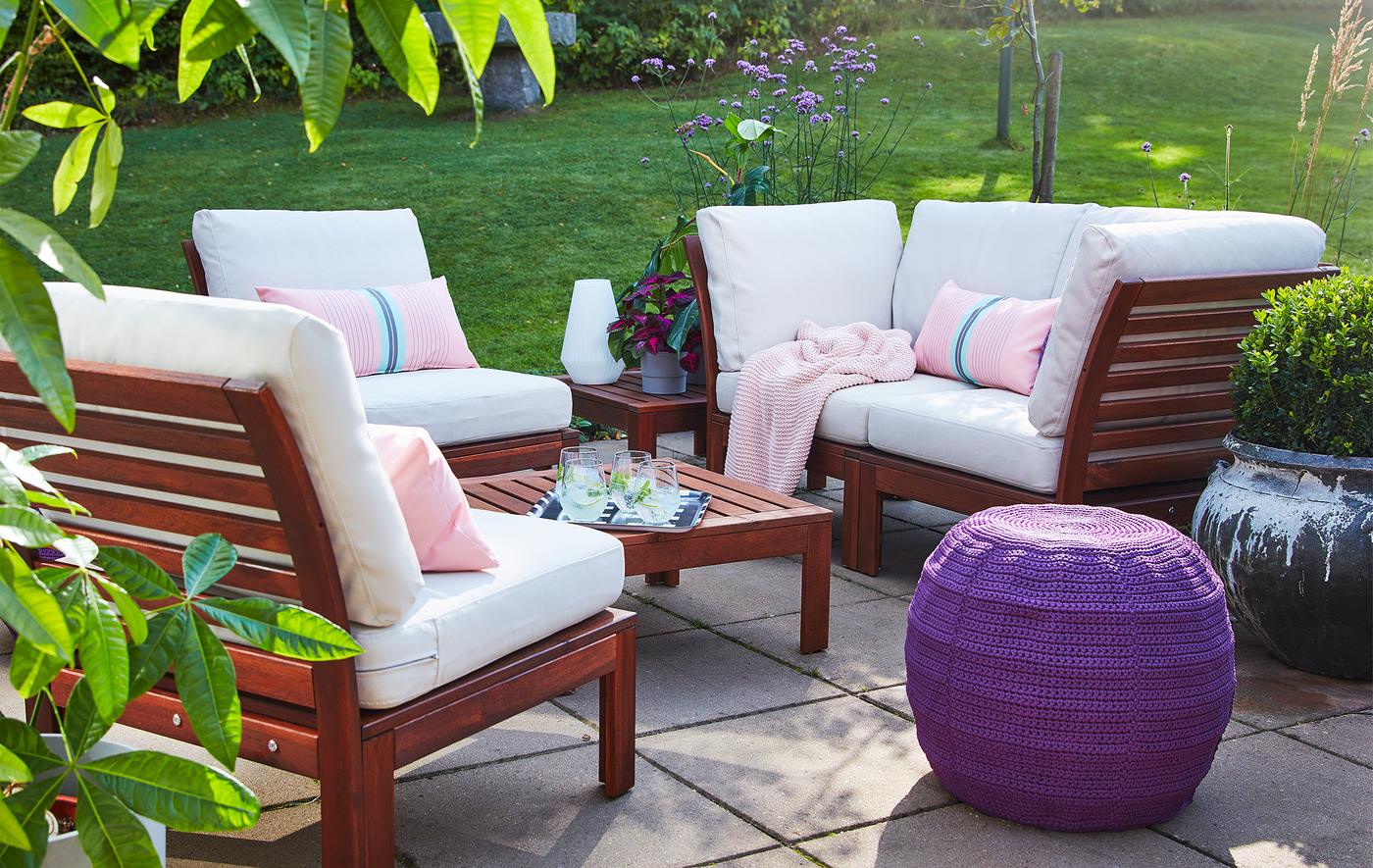 Du mobilier d’extérieur en bois avec des coussins blancs et roses, exposés sur une terrasse en pierres grises.