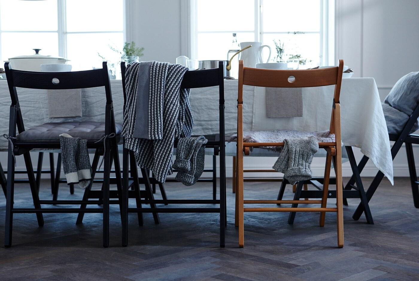 Du möchtest mit deinem festlich gedeckten Tisch beeindrucken? Mach dir auch Gedanken darüber, den Bereich unter der Tischplatte zu gestalten. Teppiche, Kissen oder Textilien um die Tischbeine sorgen für zusätzliche Feierstimmung. Hier u. a. TERJE Klappstühle in Schwarz zu sehen.