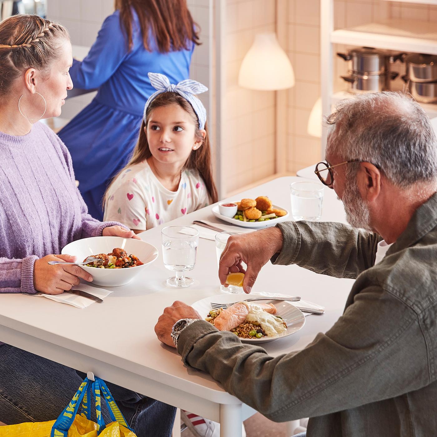 Dua orang dewasa dan seorang budak sudah hendak menikmati hidangan bersama-sama sambil duduk di meja berwarna putih di Restoran Sweden IKEA.