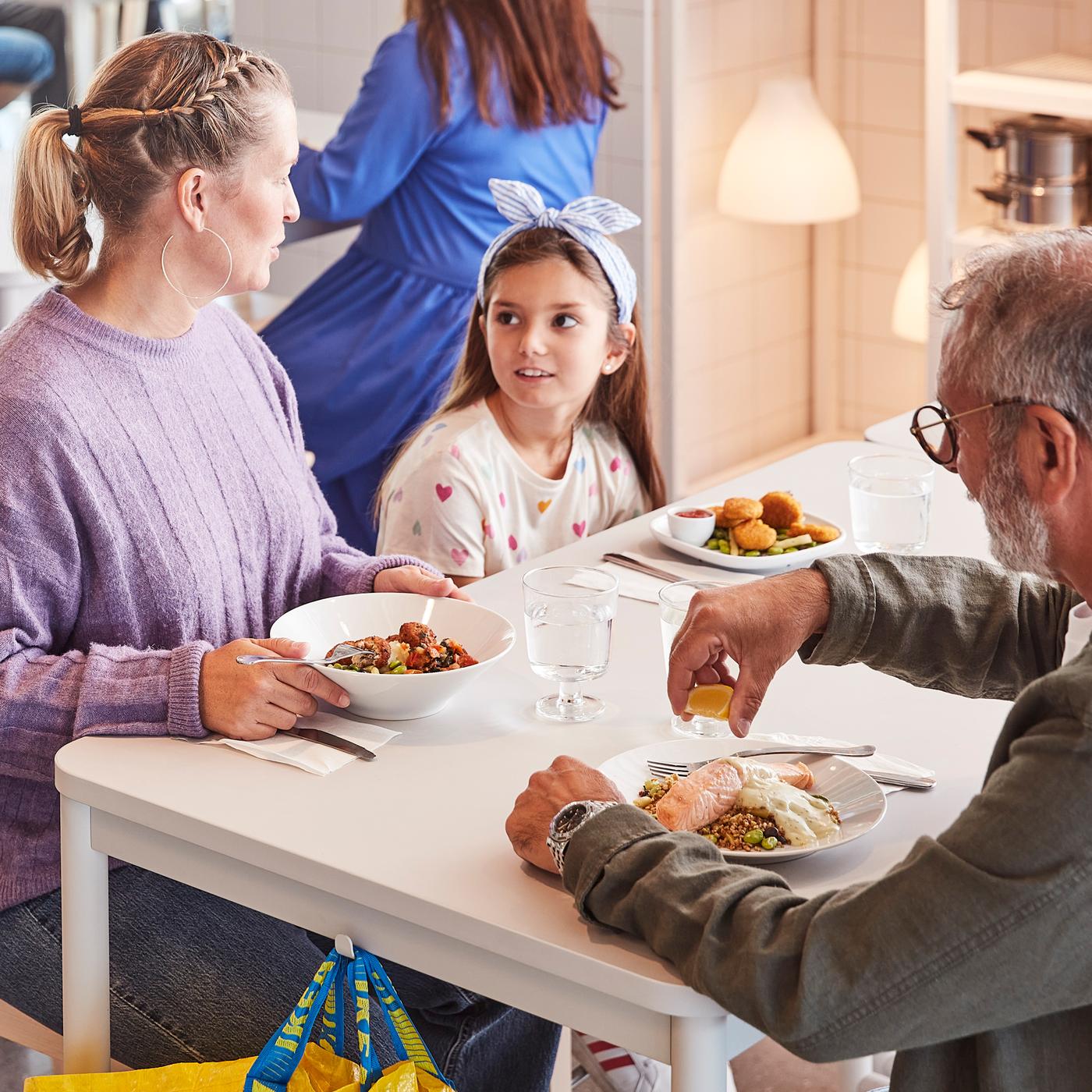 Dua orang dewasa dan seorang budak sudah hendak menikmati hidangan bersama-sama sambil duduk di meja berwarna putih di Restoran Sweden IKEA.