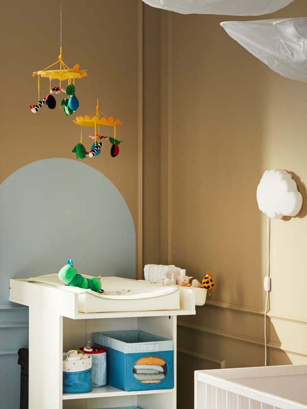 Due giostrine KLAPPA appese sopra un fasciatoio con i prodotti per il cambio del pannolino, un peluche a forma di bruco e una lampada notturna da parete - IKEA