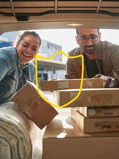 Due persone viste dall’interno di un’auto, che caricano dei pacchi IKEA nel bagagliaio