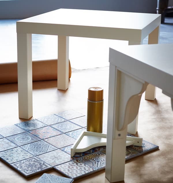 Dva bílé stolky IKEA LACK čekají na svou proměnu. Na podlaze vedle nich jsou připravené dlaždičky.