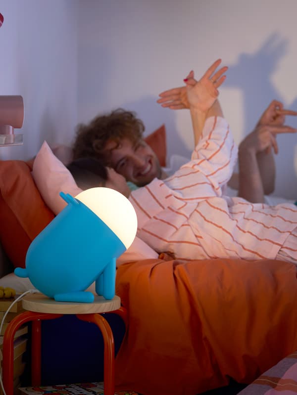 Dva mladí lidé tvoří stínové figurky zvířat pomocí rukou a modré stolní lampy ve tvaru psa GREJSIMOJS.