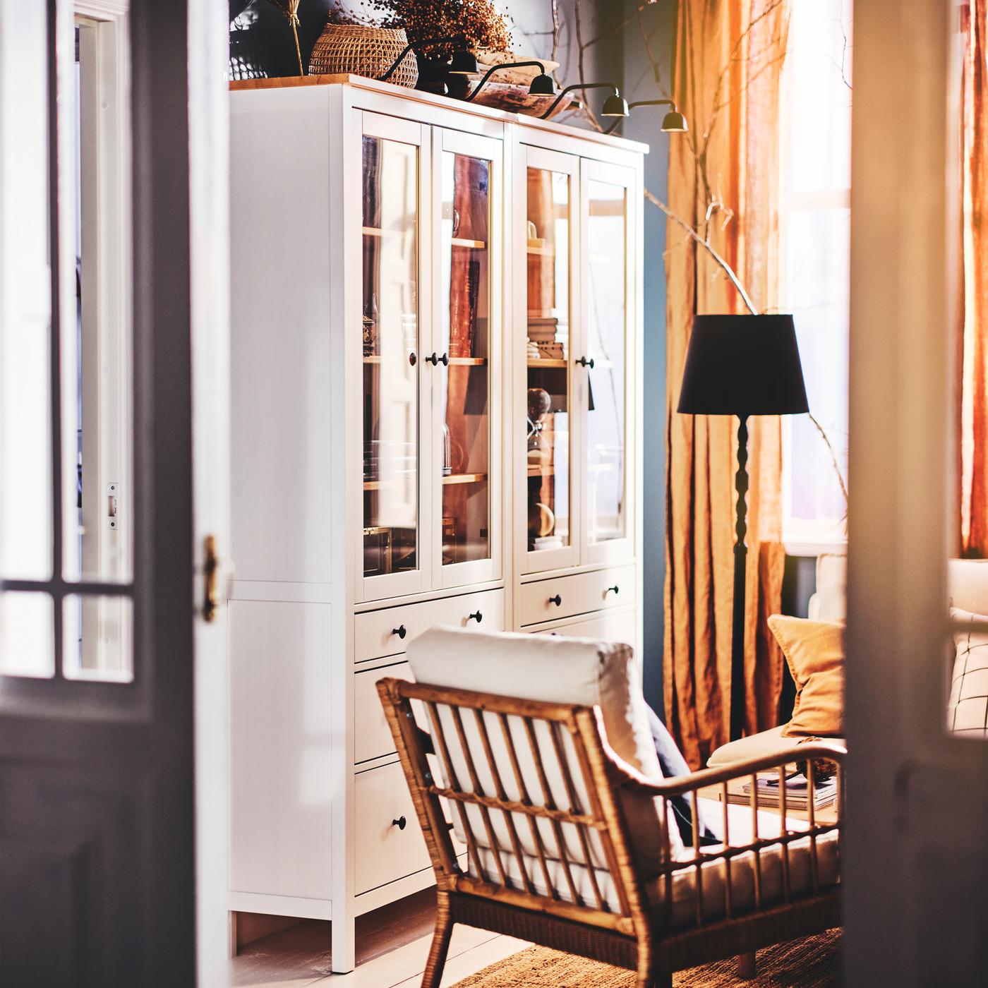 Dve bele HEMNES vitrine s tri fioke, s četiri TVÄRDRAG rasvete za kuhinjske elemente na vrhu i foteljom na tepihu.
