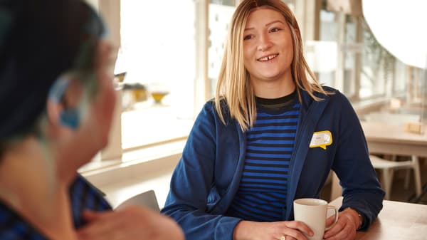 Dve IKEA zaposlene u plavim uniformama uživaju na pauzi u kantini za zaposlene.