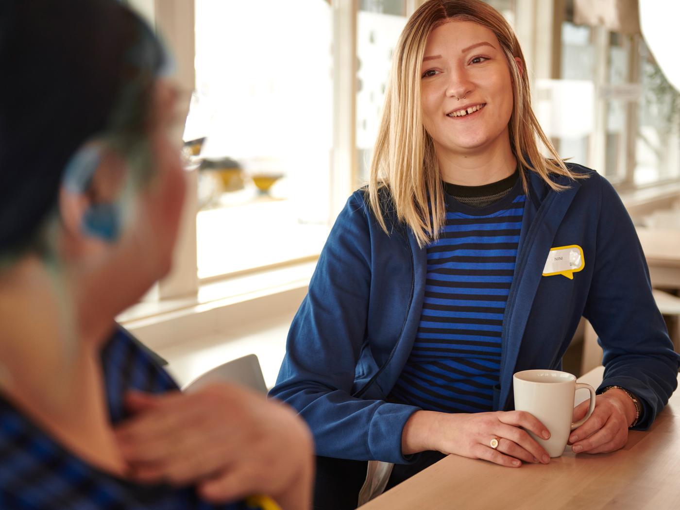 Dvoje IKEA zaposlenih, u IKEA uniformama, ispijaju kafu u kantini za zaposlene.