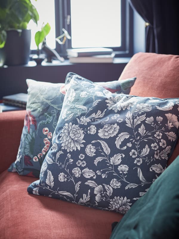 Ecke eines roten GRÖNLID Sofas, u. a. mit einem IDALINNEA Kissenbezug und anderen Exemplaren in ähnlichen Farben.