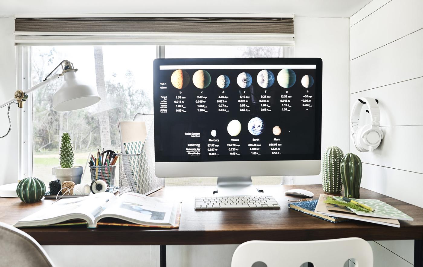 Écran d’ordinateur sur un bureau, avec cahiers, classeurs et une lampe.