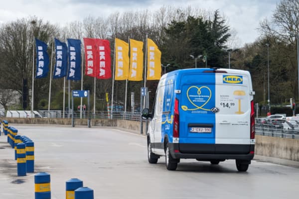 Een IKEA bestelwagen op een parkeerterrein met IKEA vlaggen zichtbaar op de achtergrond.