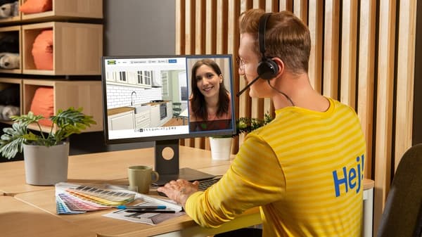 Een man zit aan een bureau en voert een videogesprek met een vrouw via een computer. Een tweede scherm toont beelden van kamerinterieurs.