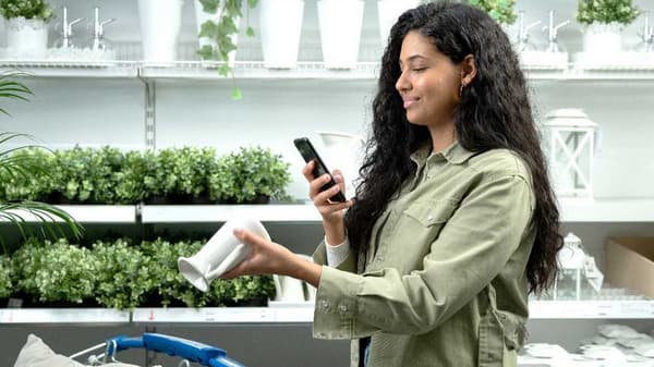 Een persoon in een winkel houdt een telefoon en een witte bloempot vast.