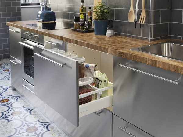 Een roestvrijstalen keuken met een houten werkblad in eiken/fineer. In een open lade wordt veel droge voeding bewaard.