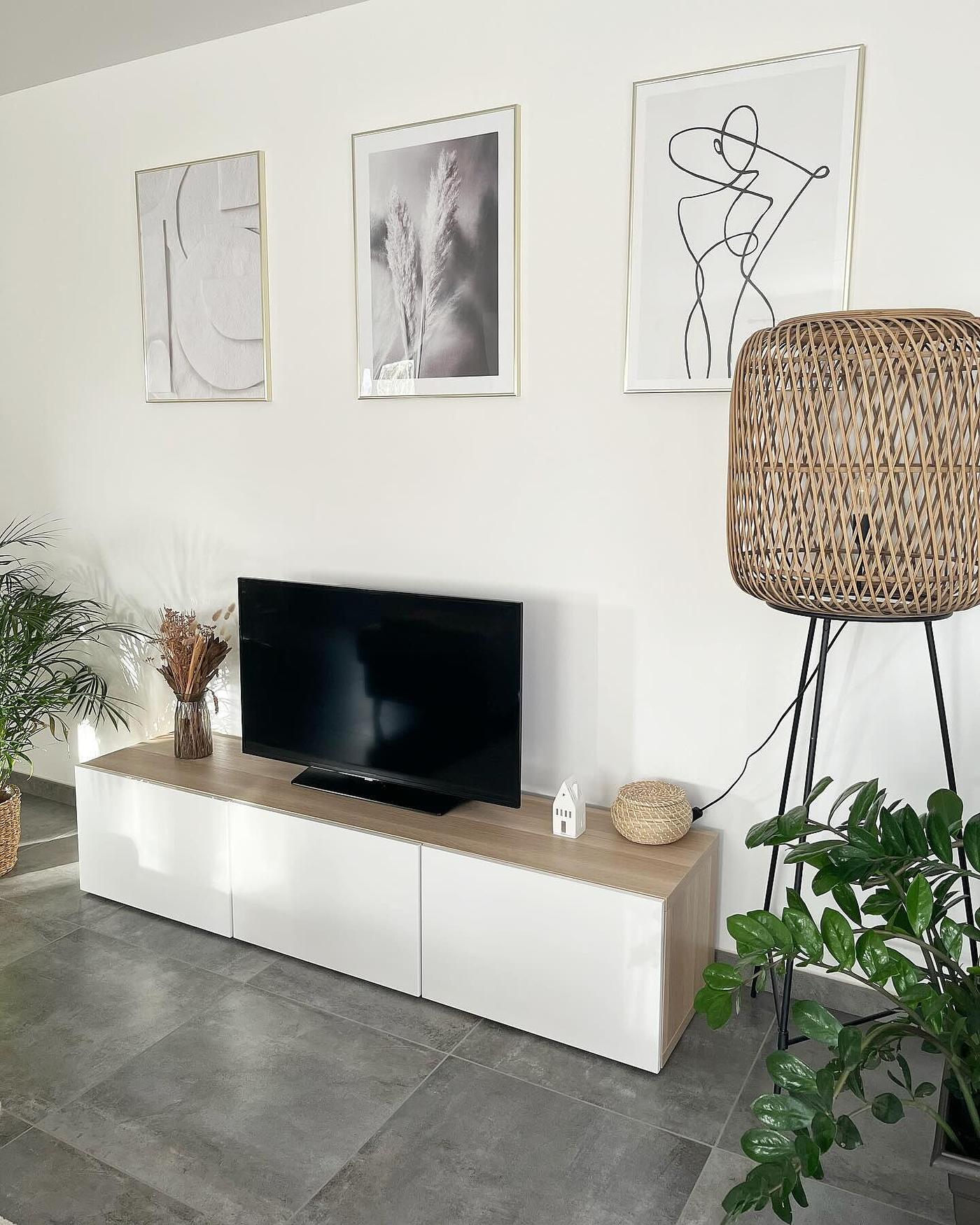 Een wit BESTÅ tv-meubel met een eikenfineer bovenblad tegen een witte muur in een lichte woonkamer.
