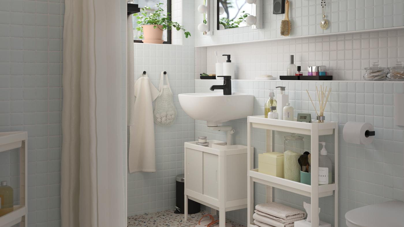 Een wit LILLTJÄRN/SKATSJÖN badkamermeubel met een SALJEN kraan langs een witte VESKEN roltafel met toiletartikelen.