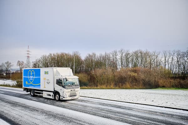 Een witte IKEA vrachtwagen met reclame rijdt op een besneeuwde weg, wintertafereel met kale bomen op de achtergrond.