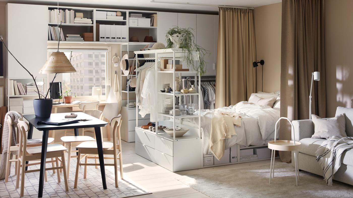 Een zonnige studioflat met witte PLATSA opbergcombinatie en bedframe, een zwarte LISABO tafel en RÖNNIGE stoelen.