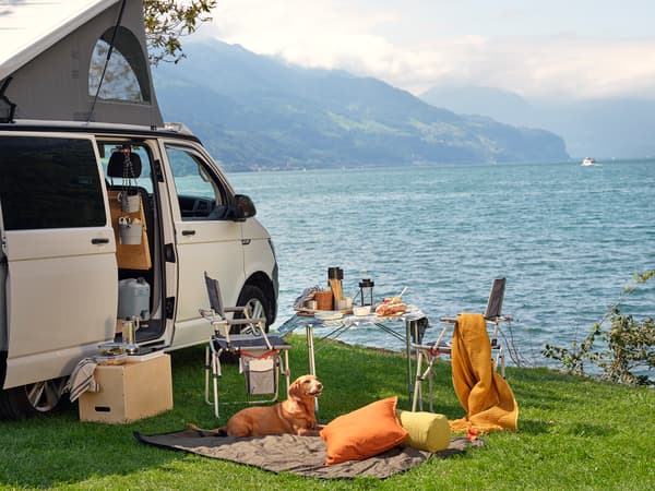 Ein am See geparkter Lieferwagen mit einem Tisch und Klappstühlen daneben.