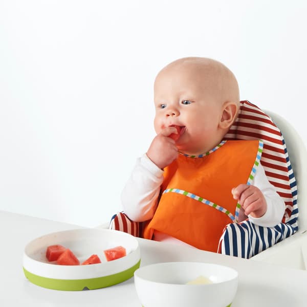 Ein Baby sitzt im Hochstuhl und isst Wassermelone.