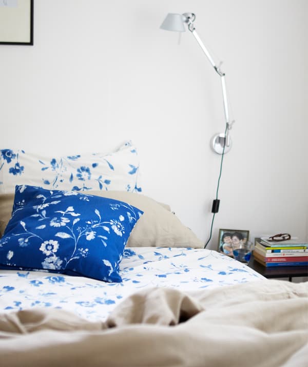 Ein Bett mit blau und weiss geblümter Bettwäsche, u. a. mit einem BLÅGRAN Kissenbezug in Blau/Weiss