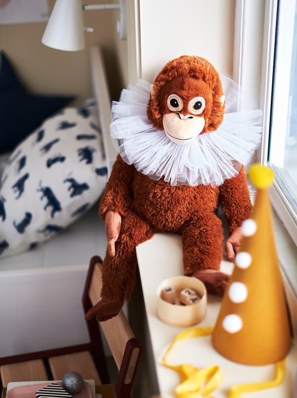 Ein DJUNGELSKOG Stofftier in Form eines Orang-Utans sitzt auf einer Fensterbank neben einem Bett im Kinderzimmer.