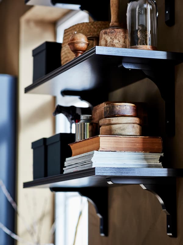 Ein dunkles BERGSHULT/RAMSHULT Wandregal mit Zeitschriften, Büchern, Boxen und anderer Aufbewahrung.