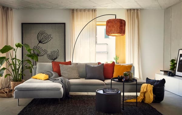 Ein Ecksofa mit verschiedenfarbigen Kissen und Beistell-Tischchen davor steht inmitten eines Wohnzimmers