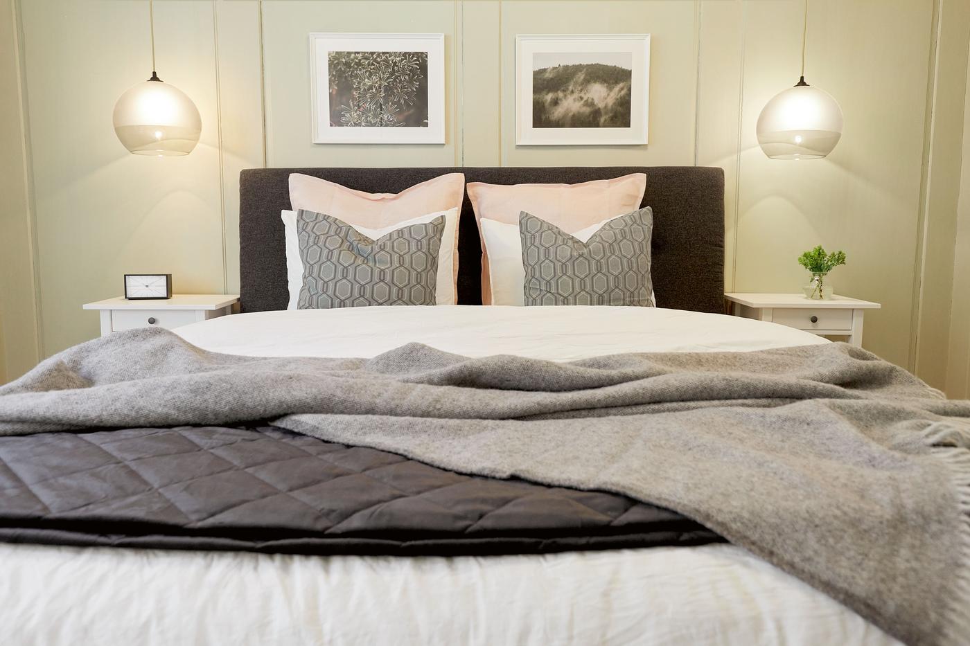 Ein frisch gemachtes Bett im Schlafzimmer mit verschiedenen Kissen, daneben Nachttische und darüber Beleuchtung