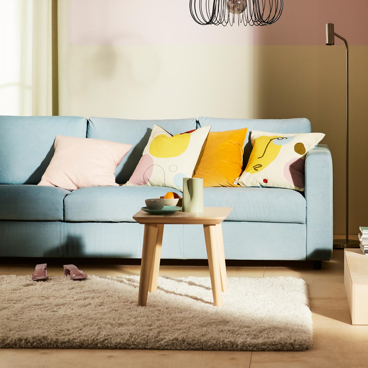 Ein hellblaues VIMLE 3er-Sofa mit bunten Kissen und einem hochflorigen VOLLERSLEV Teppich davor.