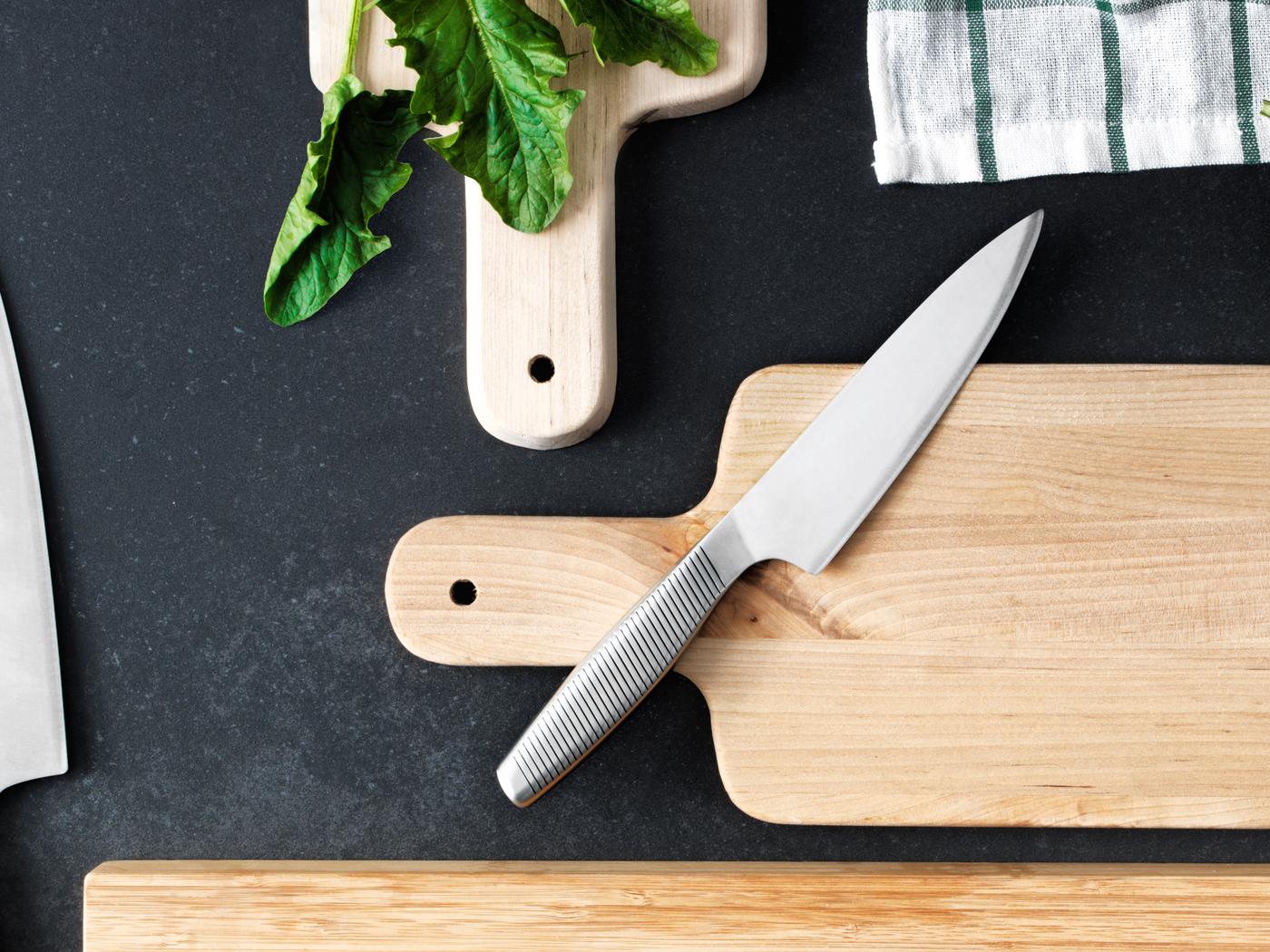Ein IKEA 365+ Kochmesser in Edelstahl liegt auf einem Schneidebrett aus Holz, das sich neben zwei anderen Schneidebrettern aus Holz befindet. 